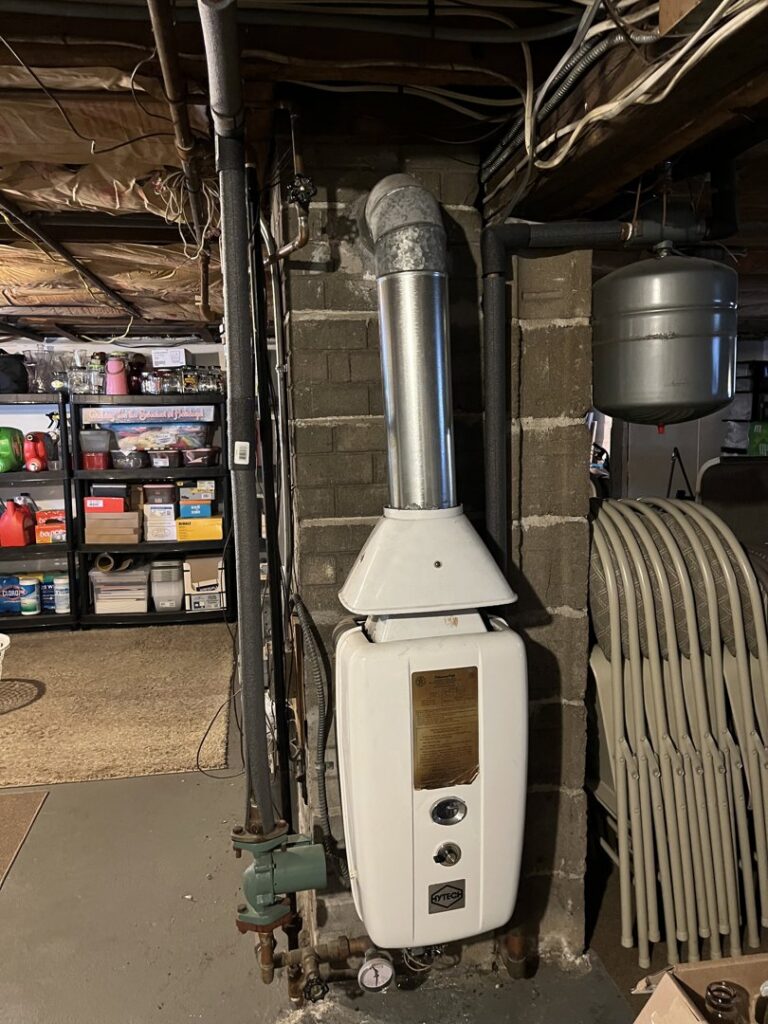 An old water heater or boiler unit with a flue pipe in a basement by Hampden County HVAC Inc. in Indian Orchard, MA