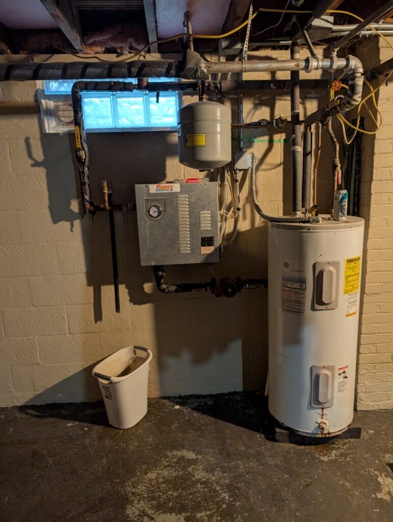 An older water heater and associated piping system in a basement, typical equipment serviced by Voegeli Heating & A/C, Inc. in Toledo, OH.