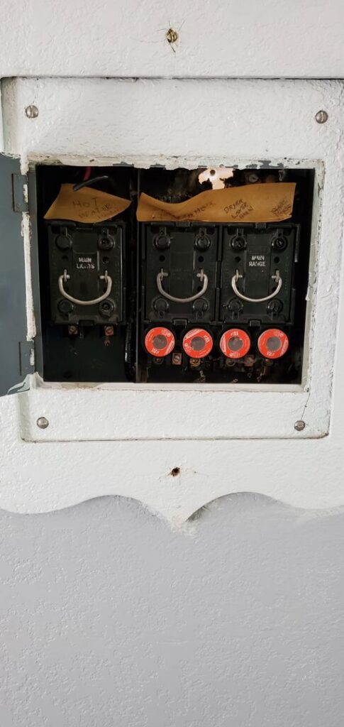 An older electrical fuse box with round fuses and main switches, representing a system that Devaney Electric Co. in Lacey, WA can service or upgrade.