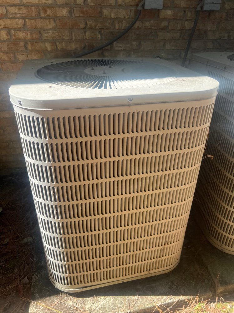 An older model outdoor AC unit next to a brick wall, representing services by Dodson A/C & Appliance in Biloxi, MS.