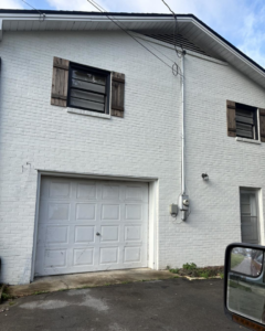 An older white garage door on a white brick house, ready for replacement by Gilliam Services LLC in Johnson City, TN.