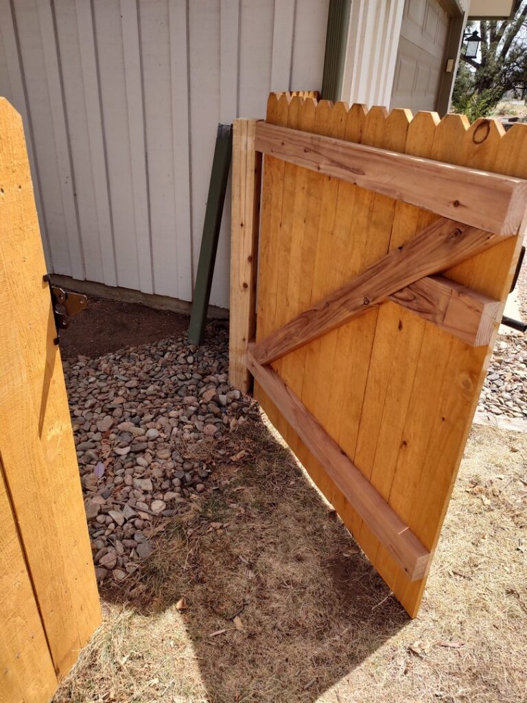An open, newly installed wood gate next to a house, showcasing the quality work of Good Neighbor Fencing, LLC in Colorado Springs, CO.