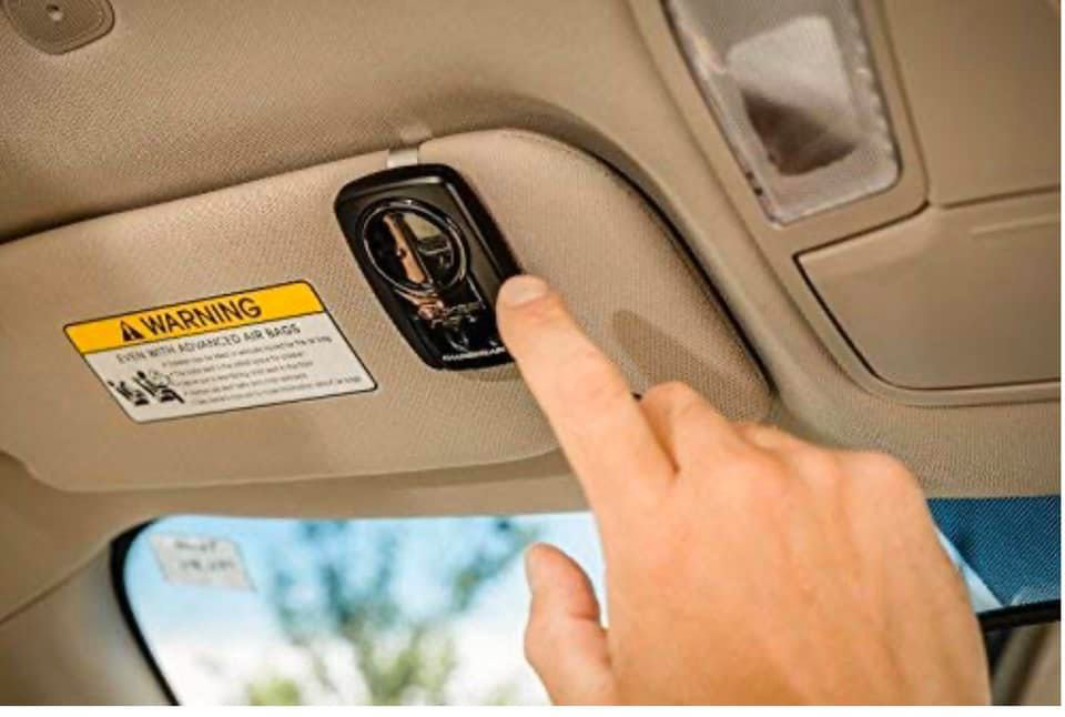 A hand operating a garage door opener remote mounted on a car's visor by Tulsa Garage Door Doctor LLC in Tulsa, OK