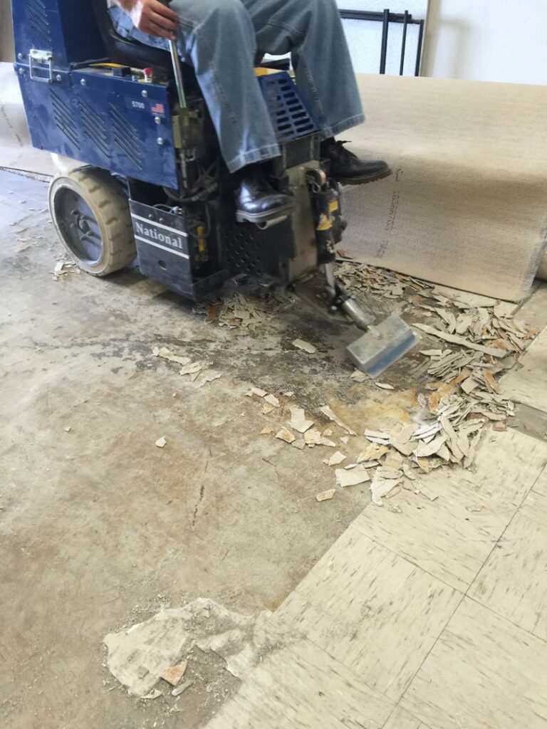 An operator removing old flooring with a machine, next to a large roll of removed carpet at Clean Site Flooring Removal in Sacramento, CA.