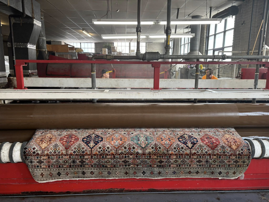 An oriental rug being fed into an industrial cleaning machine at Harb's Carpeting & Oriental Rugs in Knoxville, TN