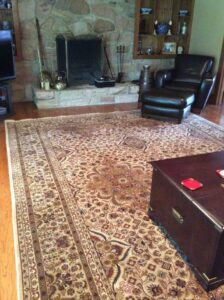 A large oriental rug complementing a living room with a stone fireplace and leather furniture, installed by Brandon Oriental Rugs, Furlong, PA.