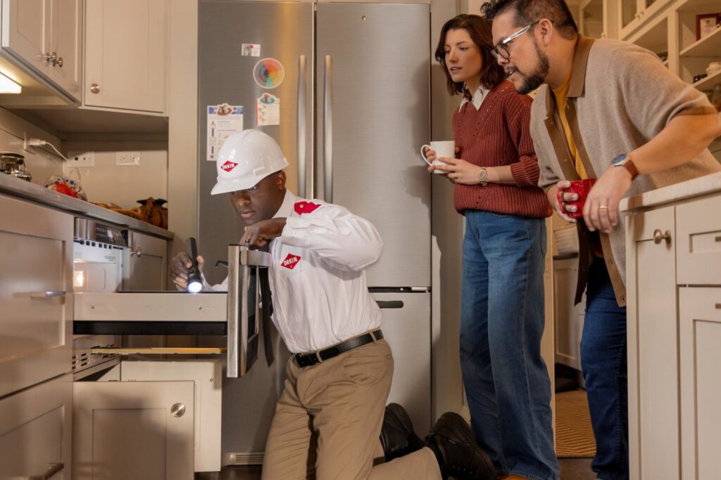 An Orkin Therm Insulation employee inspecting under a kitchen cabinet with a flashlight for pests in Harrisburg, PA.