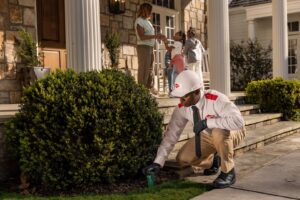 An Orkin Pest Control technician treating the ground near a bush outside a home in Austin, TX.