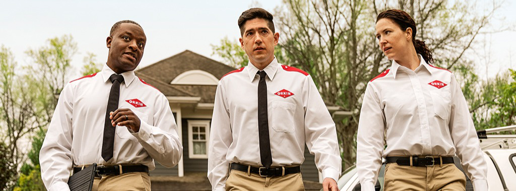Three Orkin Pest Control technicians in uniform walking towards a job site in Austin, TX.