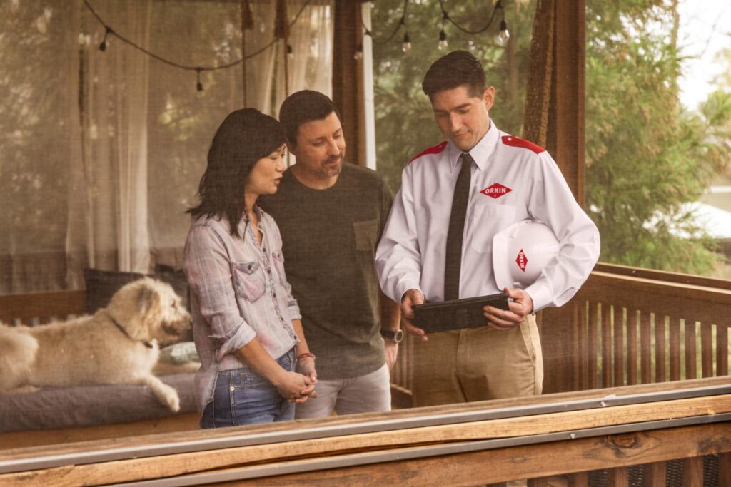 An Orkin Pest Control technician consulting with homeowners on their porch in Jonesboro, AR, discussing pest control solutions.
