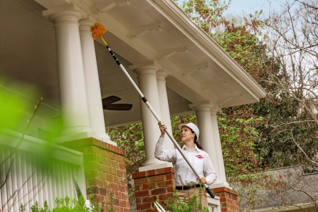 An Orkin Pest Control technician treating the eaves of a house for pests and cobwebs in Jonesboro, AR.