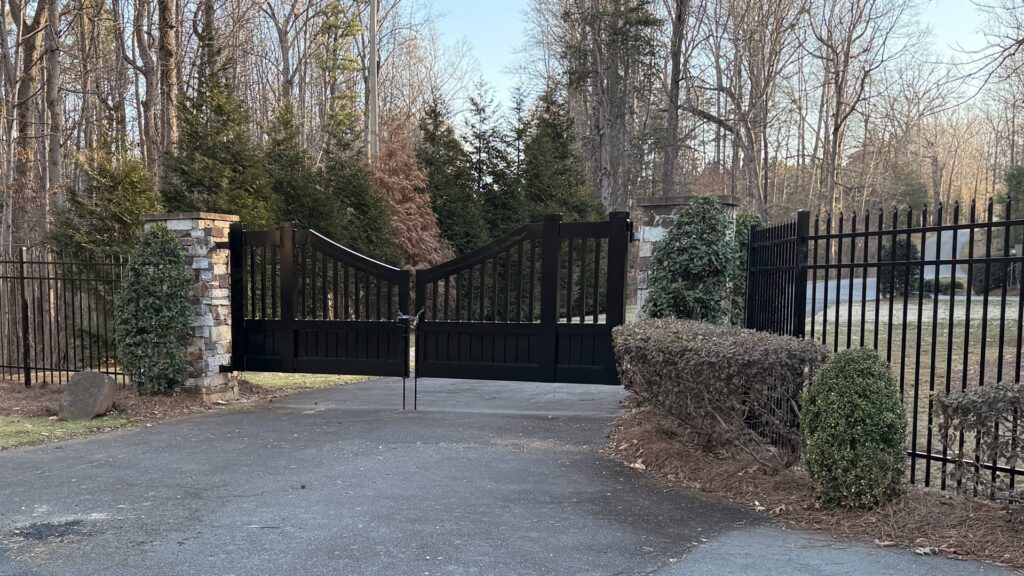 An elegant ornamental black driveway gate with stone pillars, installed by Cavitt Fencing in Concord, NC.