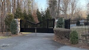 An elegant ornamental black driveway gate with stone pillars, installed by Cavitt Fencing in Concord, NC.