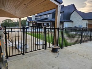 Black ornamental metal fence and gate enclosing a patio area next to a modern home, installed by QD & E Fencing in Fort Worth, TX.