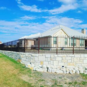Black ornamental metal fence installed on top of a decorative stone retaining wall around a residential property by QD & E Fencing in Fort Worth, TX.