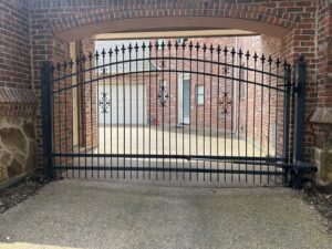 An ornate automatic black metal gate installed under a brick archway by Craftsman Automatic Gates in Dallas, TX.