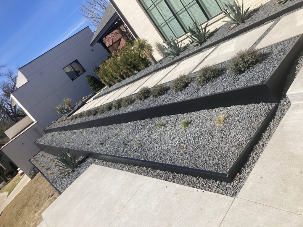 An ornate black metal automatic gate installed under a brick archway by Craftsman Automatic Gates in Dallas, TX