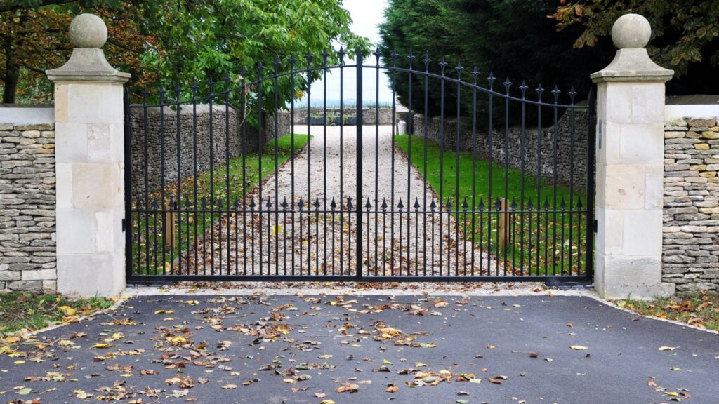 An ornate black metal driveway gate with stone pillars, installed by JH Fencing in Lawrence, KS.
