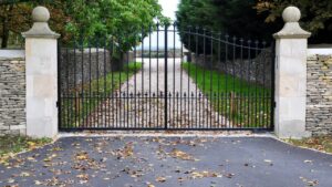 An ornate black metal driveway gate with stone pillars, installed by JH Fencing in Lawrence, KS.