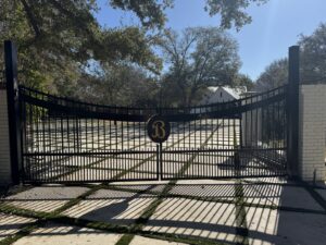An ornate black metal driveway gate with a custom monogram, installed by QD & E Fencing in Fort Worth, TX.