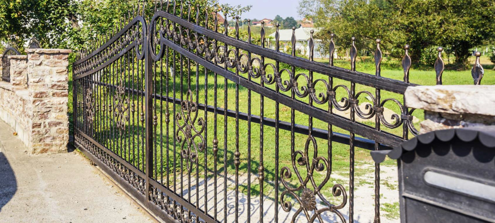 An ornate black metal fence and gate with stone pillars, showcasing work by Utah Gate Company in Salt Lake City, UT.
