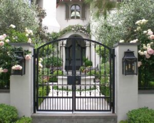 An ornate black wrought iron driveway gate in front of a large house, installed by Coastline Gate Repair in Los Angeles, CA.
