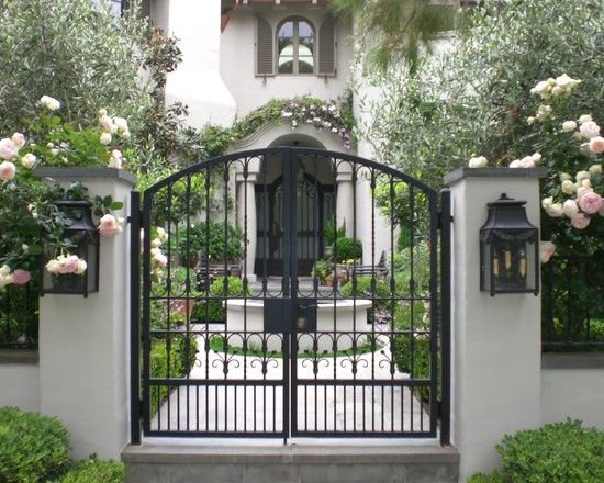 An ornate black wrought iron driveway gate in front of a large house, installed by Coastline Gate Repair in Los Angeles, CA.
