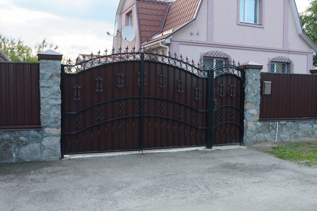 A large, ornate brown iron driveway gate with stone pillars installed by Ironcraft Welding in Chicago, IL.