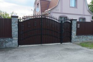 A large, ornate brown iron driveway gate with stone pillars installed by Ironcraft Welding in Chicago, IL.