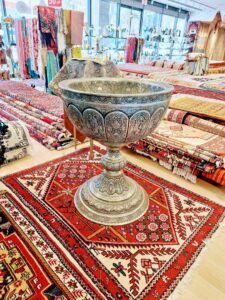 An ornate metal bowl displayed on a beautiful Persian rug at Art Of Persia, a carpet contractor in Portland, OR.