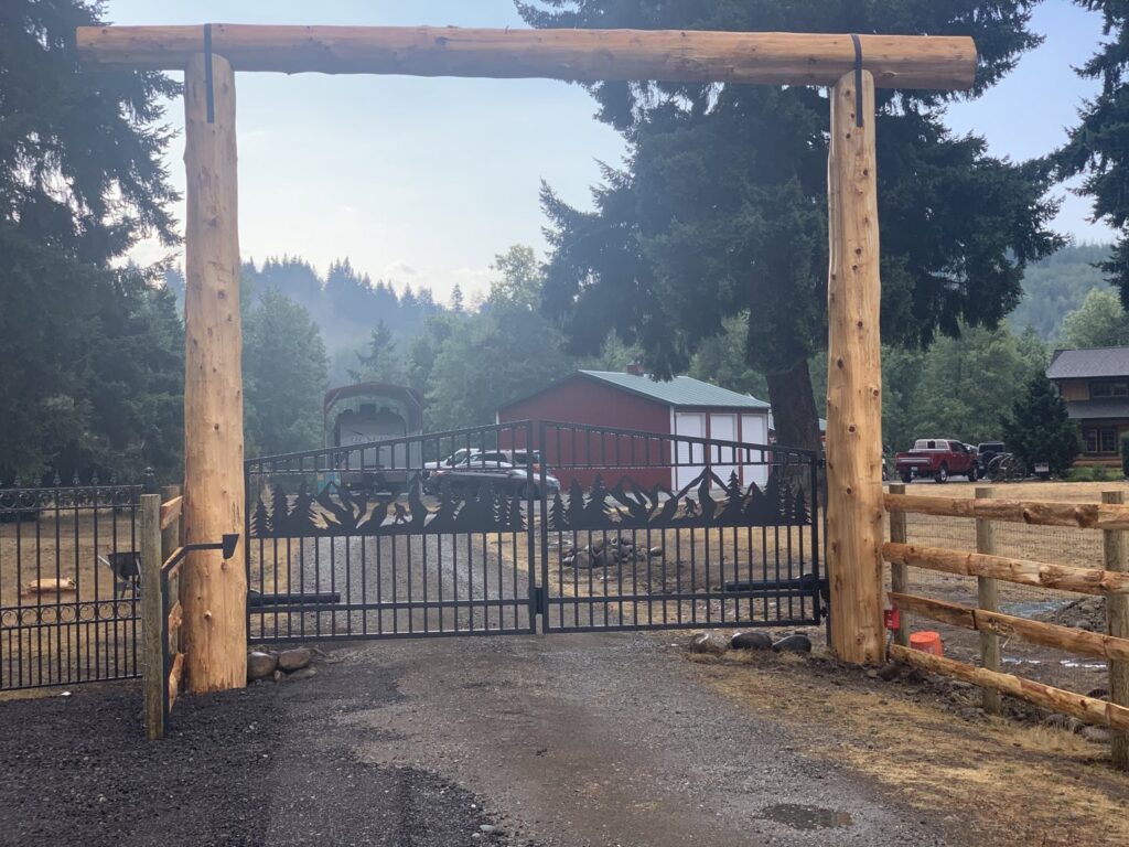 An ornate black metal gate beneath a rustic wooden archway, complemented by a split rail fence, installed by PNW FENCE in Lewiston, ID.