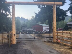 An ornate black metal gate beneath a rustic wooden archway, complemented by a split rail fence, installed by PNW FENCE in Lewiston, ID.