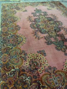 An ornate pink and multi-colored area rug laid out at the DCR AREA RUG CARE facility in Birmingham, AL, ready for professional cleaning or repair.