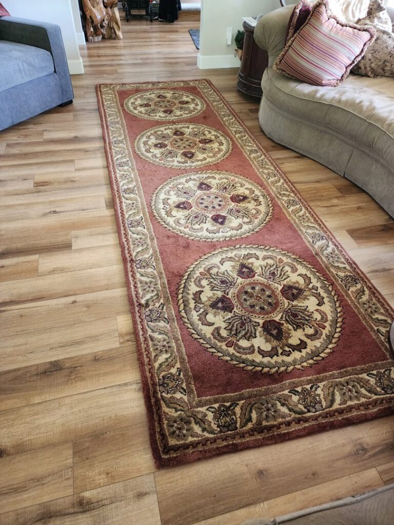 An ornate red and gold rug runner displayed on a wooden floor in a hallway by Alameda Carpet & Upholstery Cleaners in Portland, OR.