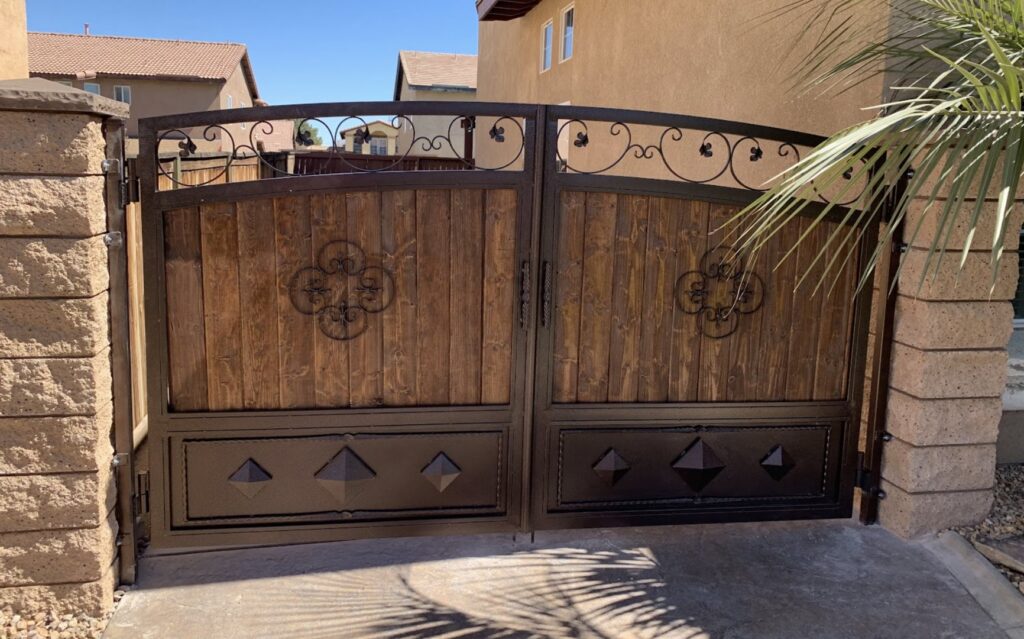 An ornate wood and wrought iron double gate flanked by stone pillars, providing an elegant entrance by True American Fence Supply and Construction in Anaheim, CA.