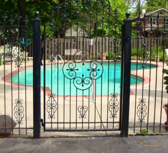 An ornate black wrought iron fence and gate enclosing a swimming pool by Kennedy Fence Corporation in St. Louis, MO.