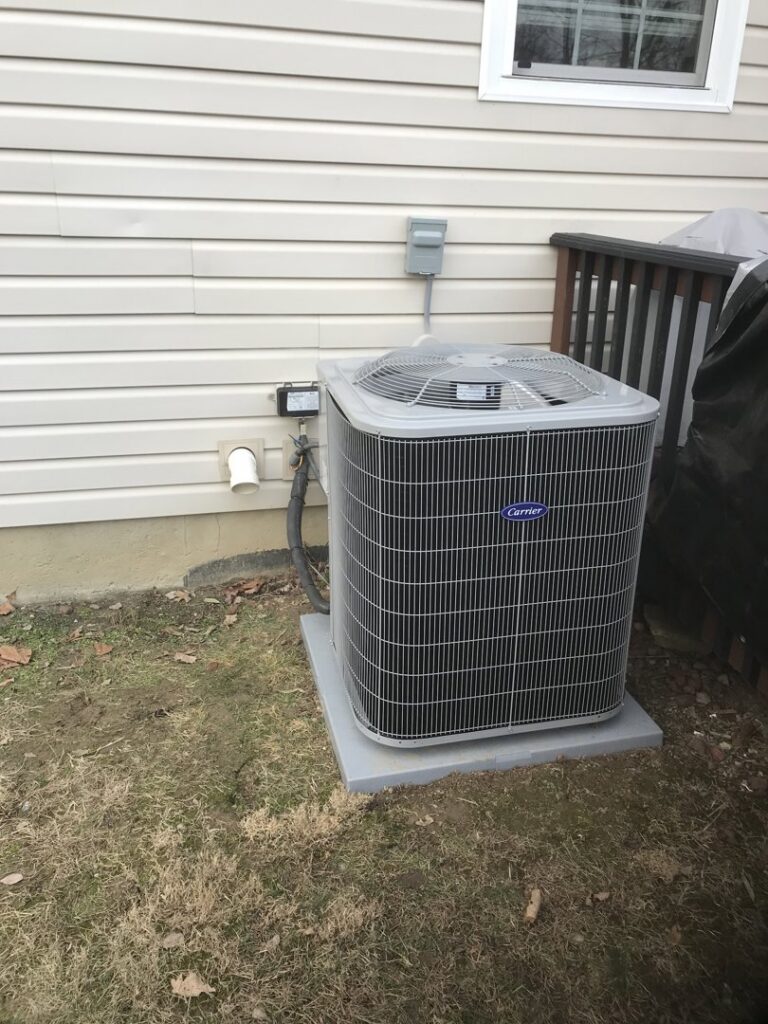 An outdoor Carrier AC condenser unit installed next to a residential building by Chad Byers - Edge Guys Heating & Cooling in Carmel, IN