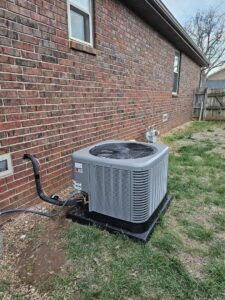 An outdoor AC condenser unit installed next to a brick house by High Efficiency HVAC in Nixa, MO.