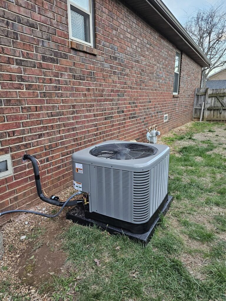 An outdoor AC condenser unit installed next to a brick house by High Efficiency HVAC in Nixa, MO.