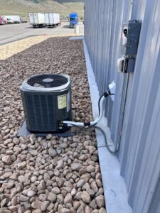An outdoor AC condenser unit installed next to a building by KCC Mechanical, LLC in Sandy, UT.