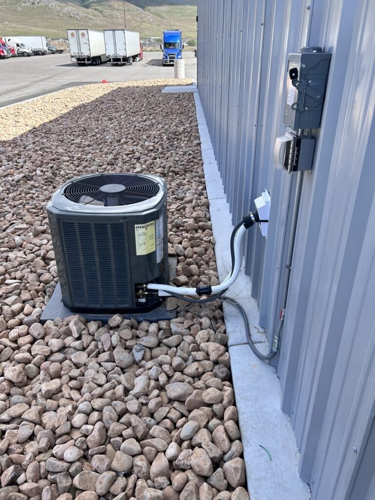 An outdoor AC condenser unit installed next to a building by KCC Mechanical, LLC in Sandy, UT.