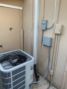 An outdoor air conditioning condenser unit installed next to a building by Lipovic Heating & Cooling in Mesa, AZ.