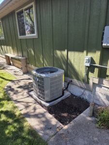 An outdoor AC condenser unit installed next to a residential building by 406 Heating & Cooling LLC in Missoula, MT.
