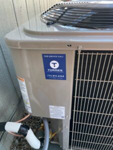 An outdoor AC condenser unit with a service sticker from Torres HVAC LLC in Reno, NV.