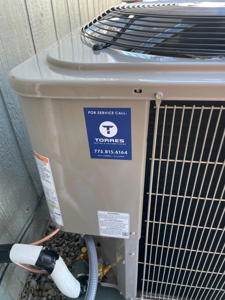 An outdoor AC condenser unit with a service sticker from Torres HVAC LLC in Reno, NV.
