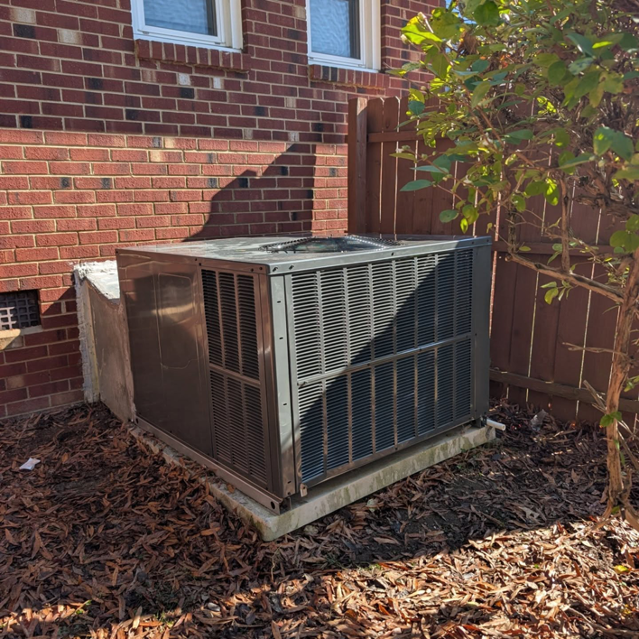 An outdoor air conditioning condenser unit installed next to a brick house by Speedy Nelson HVAC Repair in Durham, NC.