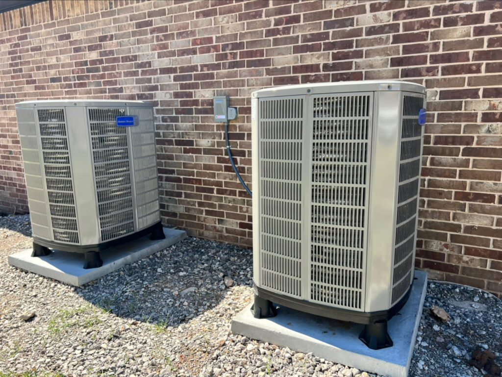 Two outdoor air conditioning condenser units installed next to a brick building by Trinity Climate Control in Goldsby, OK.
