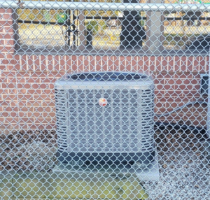 An outdoor air conditioning unit installed by Zibi Construction in Mount Prospect, IL, seen behind a fence.