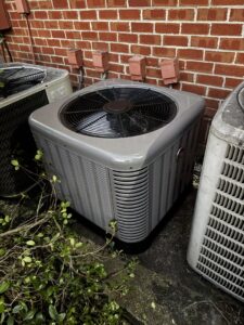 An outdoor AC unit positioned next to a brick wall, maintained by OnPoint Heating and Air in Commerce City, CO.
