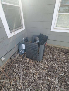 An outdoor air conditioning unit partially disassembled next to a house by Friess Heating & Air Conditioning in Topeka, KS